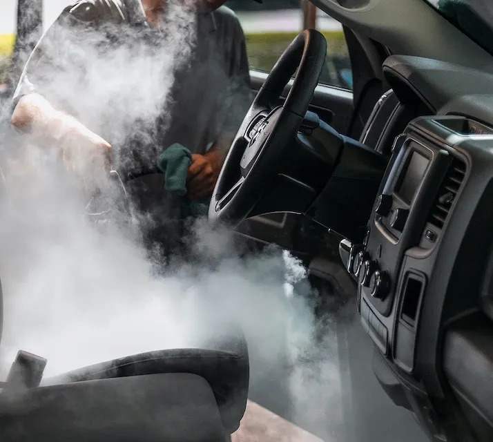 a guy steam cleaning the interior of a vehicle