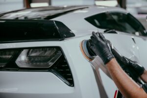 a man paint correcting a white Corvette using a polishing machine