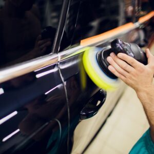 A person is polishing a black car with a sander