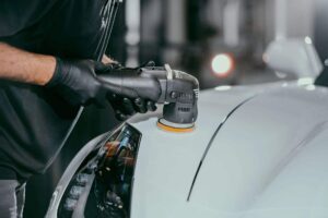 A man is polishing a white car with a machine